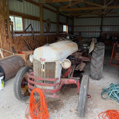 Sale Photo Thumbnail #3: Vintage Ford tractor stored in a garage, showing surface rust, age-appropriate wear, and a red front bumper guard.