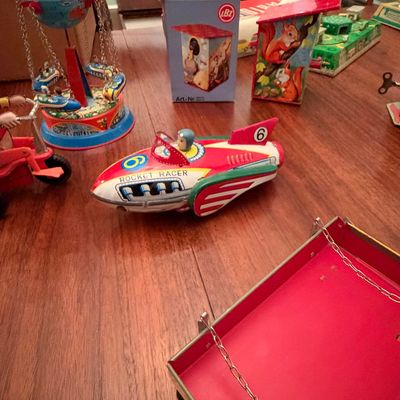 Sale Photo Thumbnail #21: Collection of vintage tin wind-up toys, including a Rocket Racer, a globe-themed carousel ride, and an LBZ boxed toy, displayed on a wooden table.