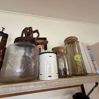 Sale Photo Thumbnail #104: Collection of vintage glass kitchenware, including a glass butter churn with cast iron gears, cork-topped storage jars, and decorative bottles.