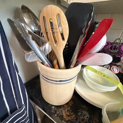 Sale Photo Thumbnail #113: Beige ceramic utensil crock with blue stripe detail, filled with various cooking utensils including spatulas, tongs, and a wooden spoon.