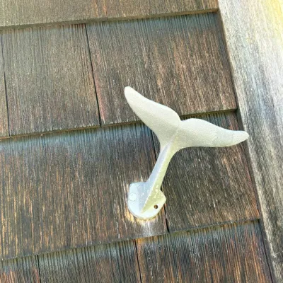 Cast aluminum whale tail wall hook or bracket mounted to weathered wood shingle siding.