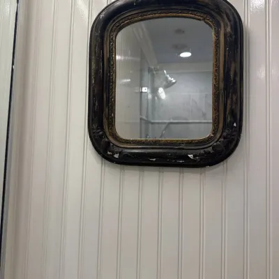 Antique small wall mirror in a distressed black and gold molded frame with carved floral corner accents.