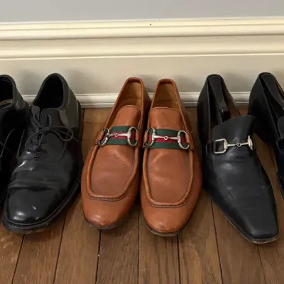 Three pairs of men's leather dress shoes, including black lace-up oxfords, tan Gucci horsebit loafers with signature web detailing,...