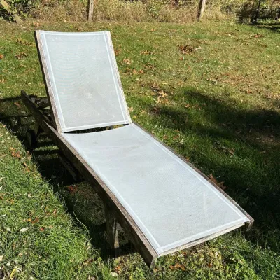 Weathered wooden patio lounge chair featuring light gray mesh sling seating and rear wheels for mobility.