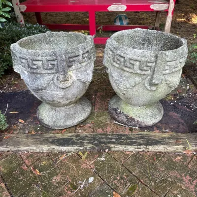 Pair of weathered concrete garden urn planters featuring Greek key trim and a pedestal base.