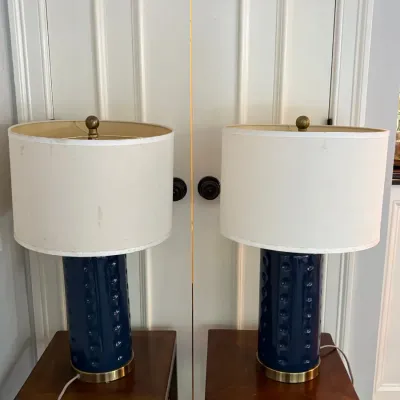 Sale Photo Thumbnail #114: Pair of contemporary navy blue glazed ceramic table lamps with brass accents and white drum shades, displayed on wooden side tables.