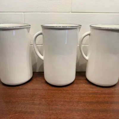 Trio of white ceramic pitchers with dark blue or black painted rims, displaying a simple farmhouse style.