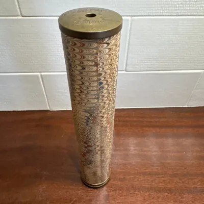 Antique style kaleidoscope with a marbled paper wrapped body and brass fittings, standing upright on a wooden surface.