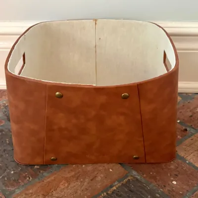 Sale Photo Thumbnail #116: Brown faux leather storage bin with brass rivet accents and cutout side handles, featuring a off-white felt interior.