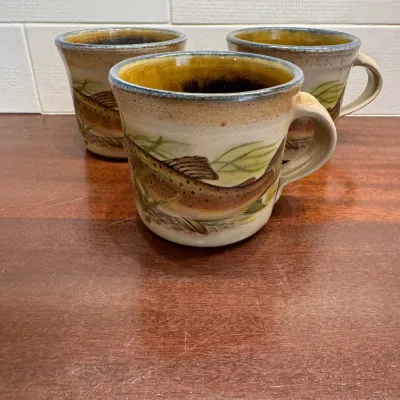 Set of three vintage studio pottery mugs featuring hand-painted trout designs and honey-yellow interior glaze.