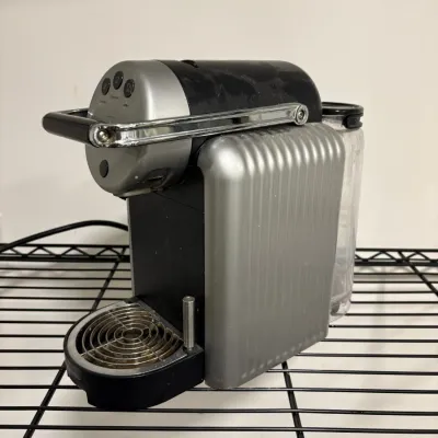 Sale Photo Thumbnail #147: Nespresso Pixie single-serve espresso machine in silver and black, showing moderate surface wear and light dust.