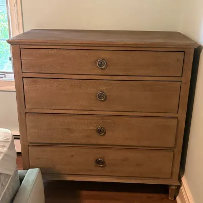 French provincial-style wooden four-drawer chest in a natural distressed finish with antique brass ring pulls.