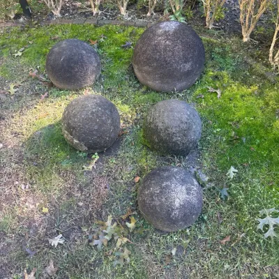 Set of five spherical concrete or stone garden ornaments resting on grass and moss.