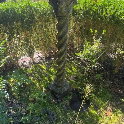 Weathered concrete garden pedestal featuring a spiral twist column and acanthus leaf capital.