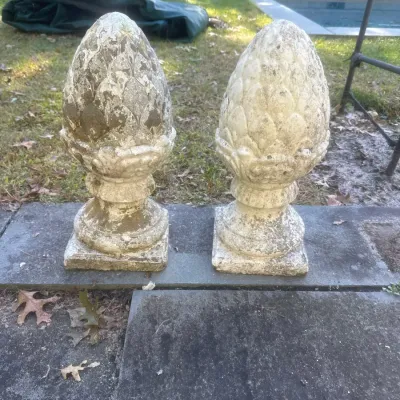 Pair of weathered concrete pinecone garden finials set on square bases, showing age-related patina and moss.
