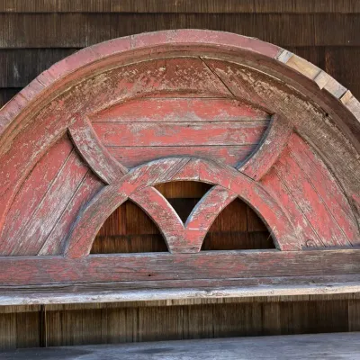Large vintage semi-circular wooden architectural salvage piece with weathered, peeling red paint and decorative curved inner framing.