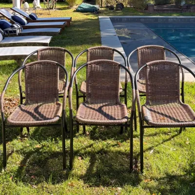 Set of six brown woven resin wicker patio chairs with dark metal frames, arranged on a lawn near a swimming pool.