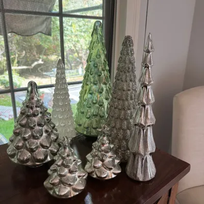 Collection of seven glass decorative Christmas trees in mercury silver, white, and green finishes, displayed on a wooden table.