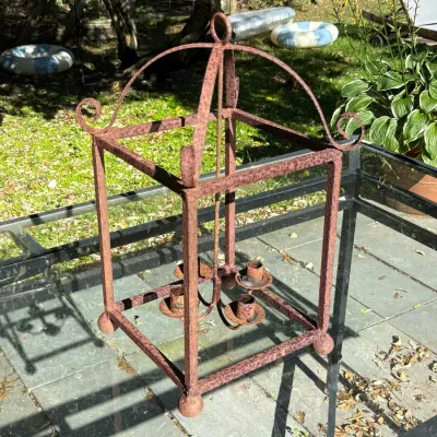Rustic wrought iron lantern-style chandelier frame featuring scrollwork accents and four candle cups, showing heavy surface rust.