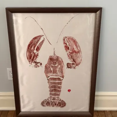 Framed gyotaku-style lobster print in reddish-brown ink on paper, displayed in a dark wooden frame.