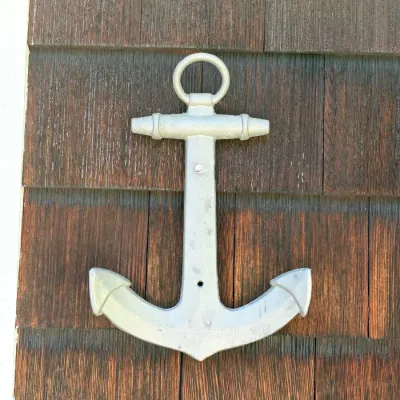 Cast metal wall-mounted anchor decor with a silver-painted finish, displayed on a wooden shingle wall.