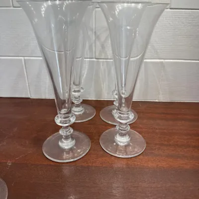 Set of four clear glass champagne flutes featuring flared trumpet-style rims and knopped stems.