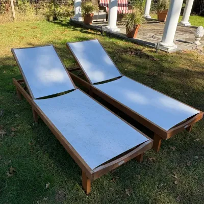 Pair of outdoor chaise lounges with wooden frames and white fabric sling seating, set in a grassy yard.