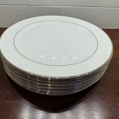 Stack of white porcelain dinner plates featuring silver or platinum metallic trim detail along the rims.
