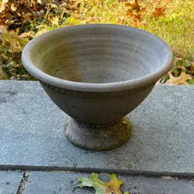 Weathered concrete pedestal urn planter featuring a wide bowl with bead trim details along the rim and base.