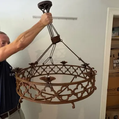 Sale Photo Thumbnail #105: Gothic Revival style wrought iron chandelier featuring a circular frame with quatrefoil decorative cutouts, multiple light sockets, and a heavily rusted patina finish.