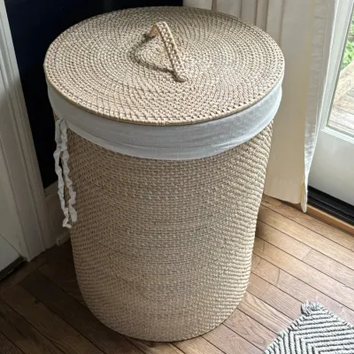 Tall cylindrical woven rattan hamper with a fitted lid and white fabric liner.