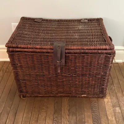 Large dark-stained wicker storage trunk featuring a hinged lid and leather strap closure with brass hardware.