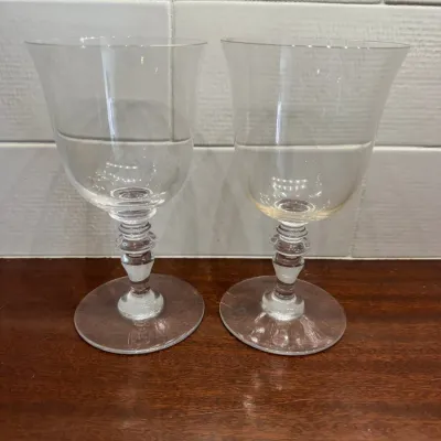Pair of clear glass goblets with knopped stems and wide circular bases, displayed on a wooden surface.