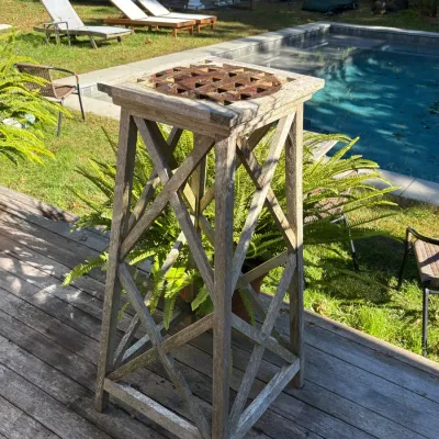 Weathered teak pedestal plant stand featuring an open crisscross lattice frame and a square top with a decorative center grate.