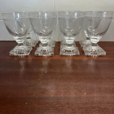 Set of eight clear glass goblets featuring delicate etched floral detailing along the rims and sturdy square bases.