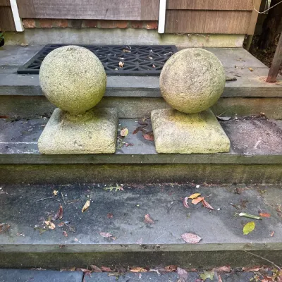 Pair of weathered concrete stone ball finials with square bases, suitable for garden or gatepost decoration.