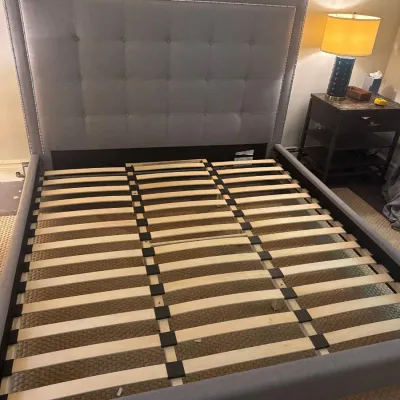 Modern upholstered platform bed frame featuring a tall grey button-tufted headboard with nailhead trim and wooden support slats.