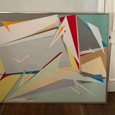 Large geometric abstract canvas painting in a silver metal floater frame, featuring dynamic angular shapes in bold and neutral tones.