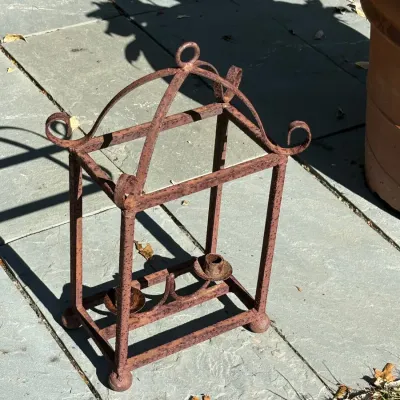 Rust-patinated wrought iron double candle holder frame with a birdcage-inspired dome top, scrollwork accents, and ball feet.