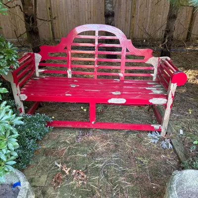 Red painted wooden garden bench featuring an arched slat back and slatted seat, showing heavy paint wear and weathering.