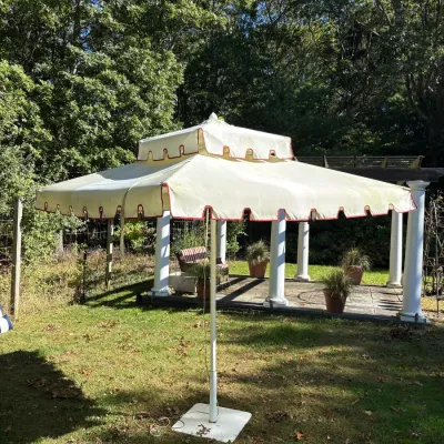 Large outdoor patio umbrella with a double-tier cream canopy, red scalloped trim, and a sturdy white metal pole with a flat square base.