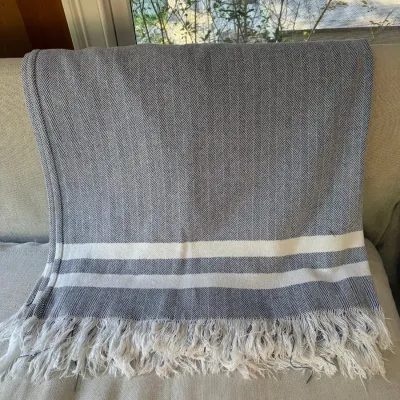 Sale Photo Thumbnail #117: Grey herringbone pattern woven throw blanket featuring white striped accents and fringed edges.