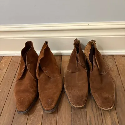Sale Photo Thumbnail #102: Two pairs of men's brown suede chukka boots resting on a hardwood floor, showing light wear and scuffing.