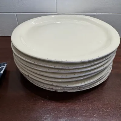 Stack of off-white ceramic dinner plates featuring subtle speckling along the edges.