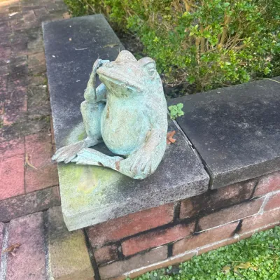 Weathered cast metal frog garden statue with verdigris patina, depicted in a seated, pensive pose.