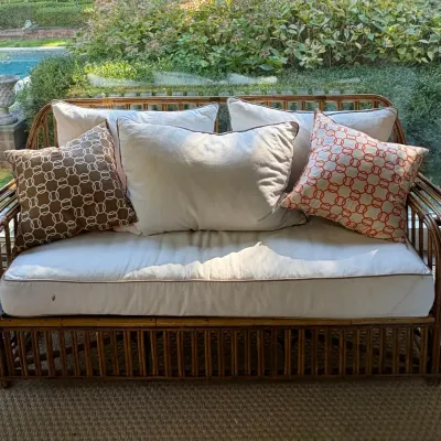 Sale Photo Thumbnail #119: Rattan or wicker loveseat with off-white seat and back cushions, accented by geometric throw pillows in brown and orange patterns.