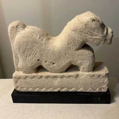 Sale Photo Thumbnail #131: Carved limestone stylized animal sculpture depicting a horse or hound, mounted on a black base.