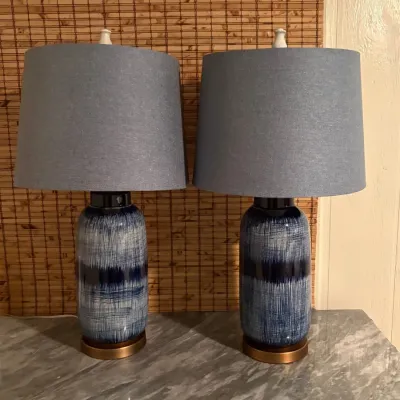 Pair of contemporary table lamps featuring blue textured ceramic bases and matching grey drum shades, set on a marble-topped surface.