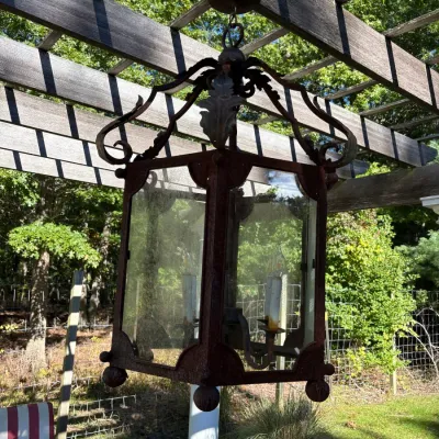 Large vintage wrought iron hanging lantern with glass side panels and candle-style lights, showing an aged patina.