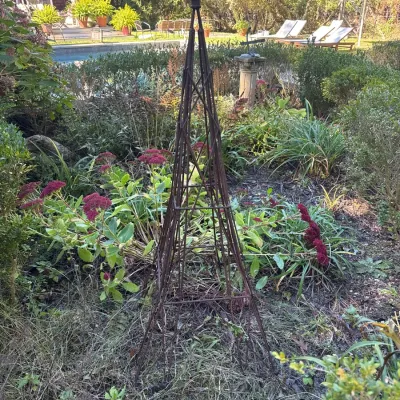 Rustic wrought iron garden obelisk trellis featuring a fleur-de-lis finial and weathered patina.